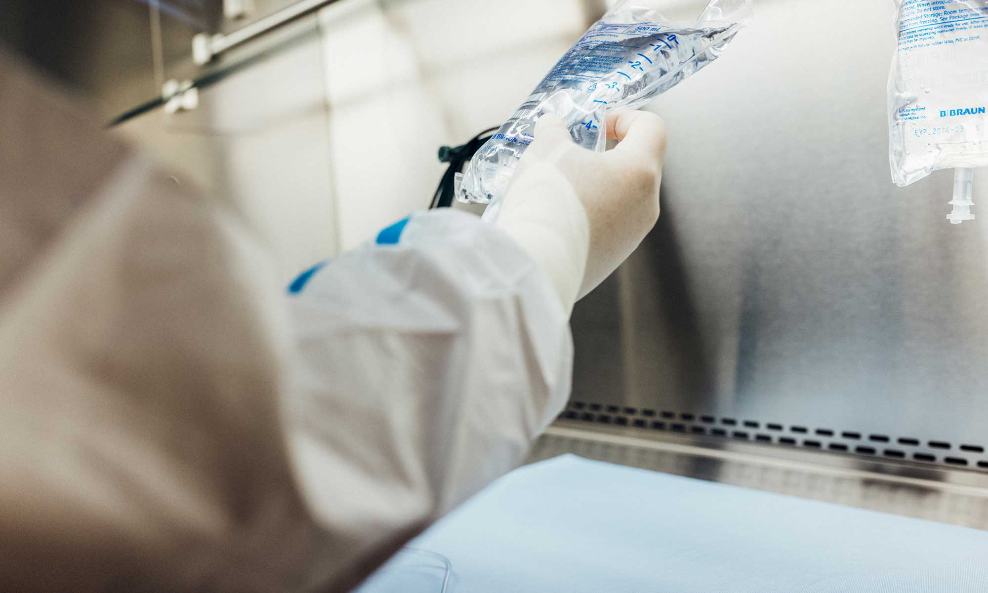 Person in a lab coat adjusts an IV bag in a clean, sterile medical environment.
