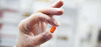 Gloved hand holding small orange pill