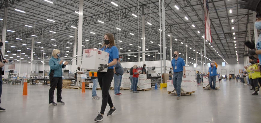 Distribution workers carry labeled and processed COVID-19 vaccine doses to the shipping area at McKesson’s Louisville, Ky. location