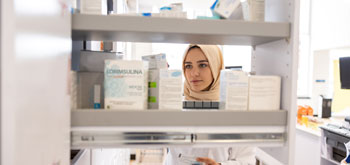 A female pharmacist wearing a hijab looks through medications on shelves