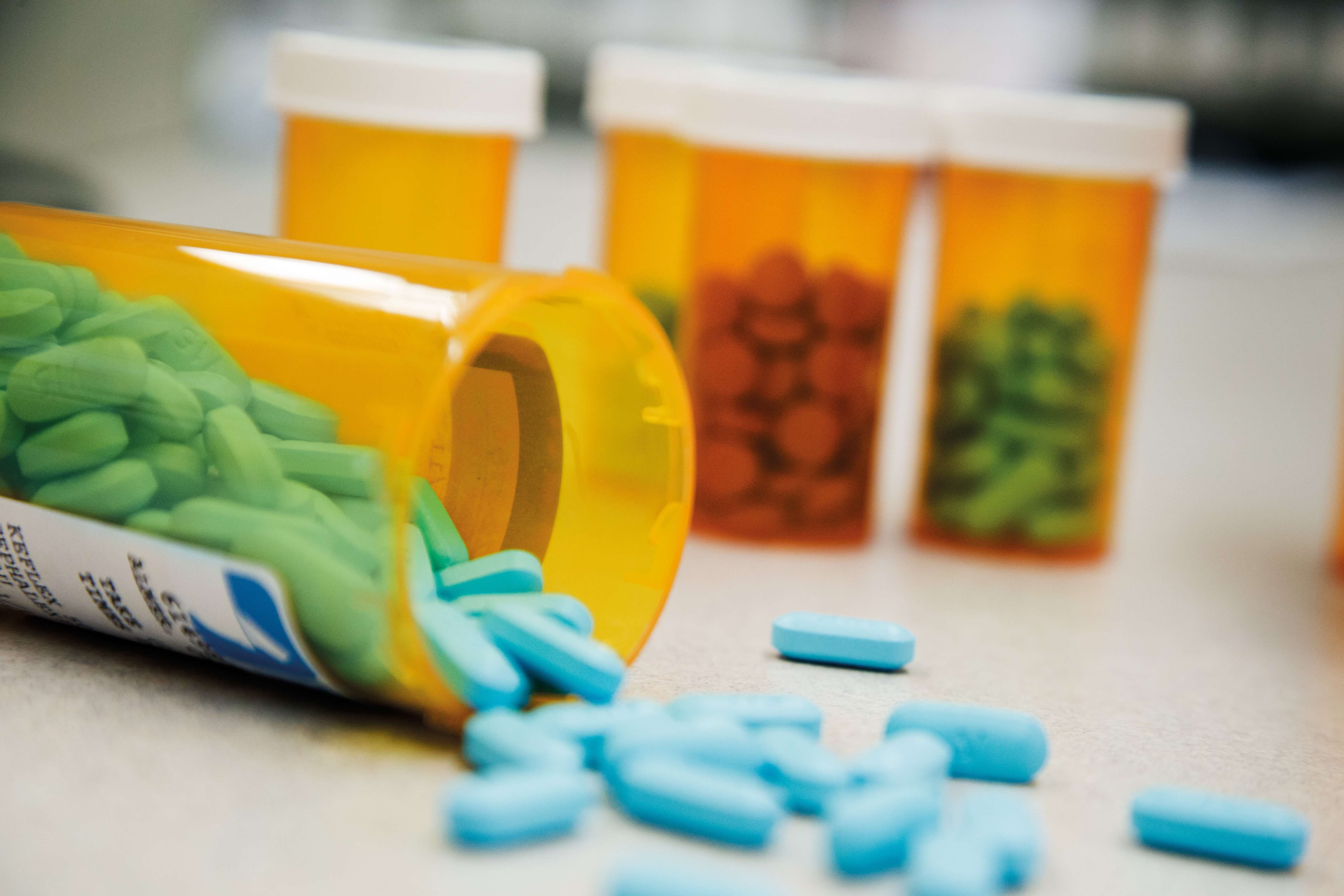 Spilled blue pills from an orange prescription bottle with more bottles in the background.