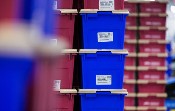 Stacked blue and red bins with barcode labels in a warehouse aisle.