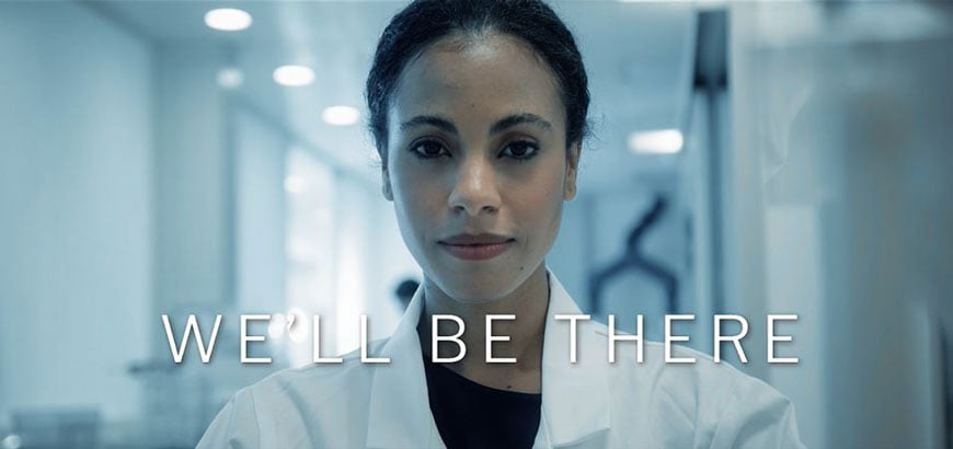 Pharmacist looking at the camera with the title "We'll Be There" over the image.