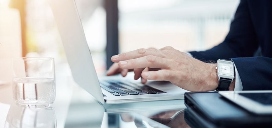 A close up image of hands typing on a keyboard at a desk