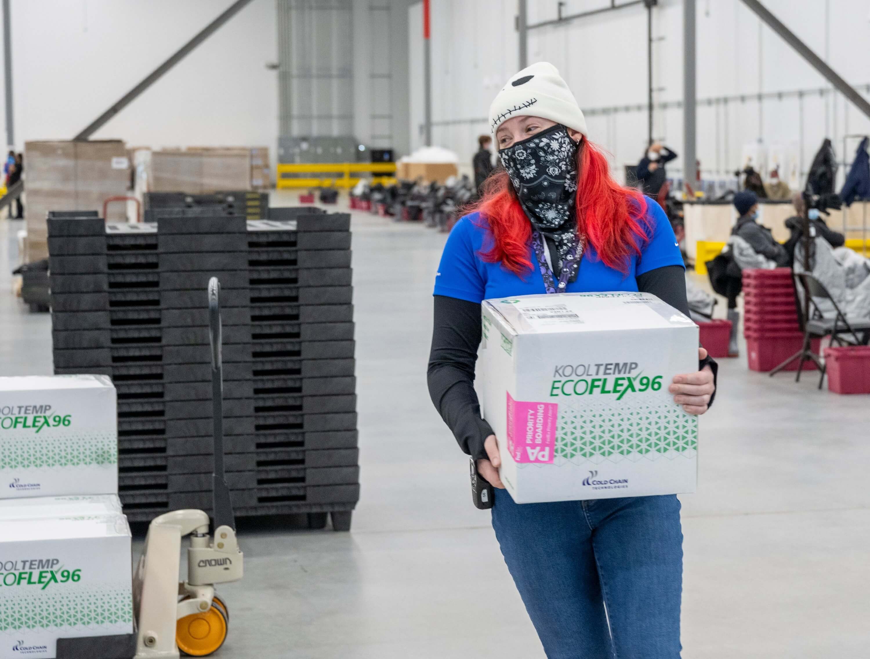 Person in a warehouse carrying a box labeled 'KoolTemp EcoFlex 96' with other boxes and equipment in the background.
