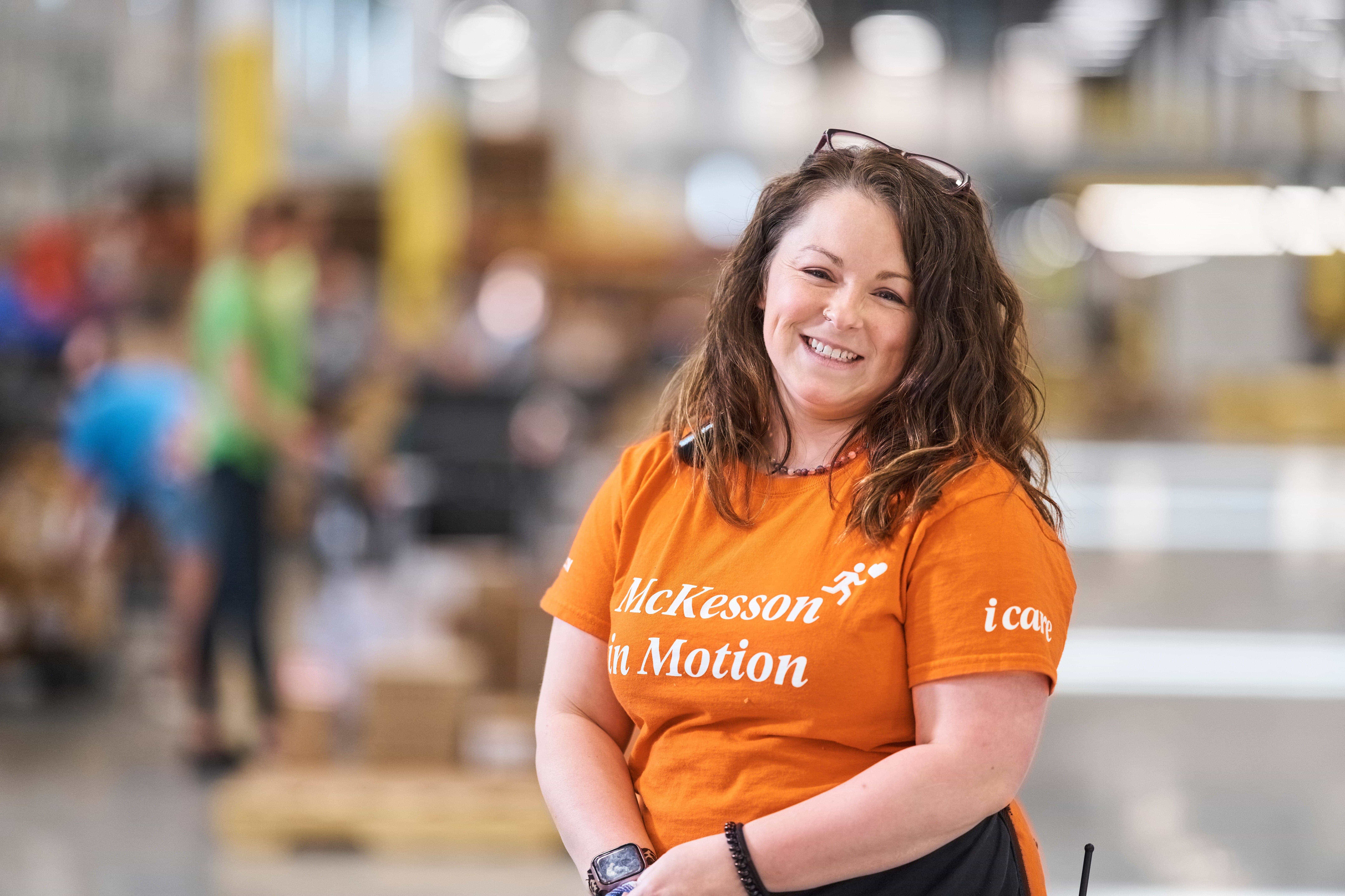 Person wearing an orange "McKesson in Motion" t-shirt standing in a warehouse with blurred background.