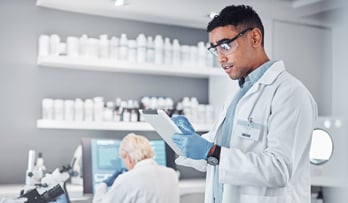 Two scientists in lab coats work in a laboratory with microscopes and computers.
