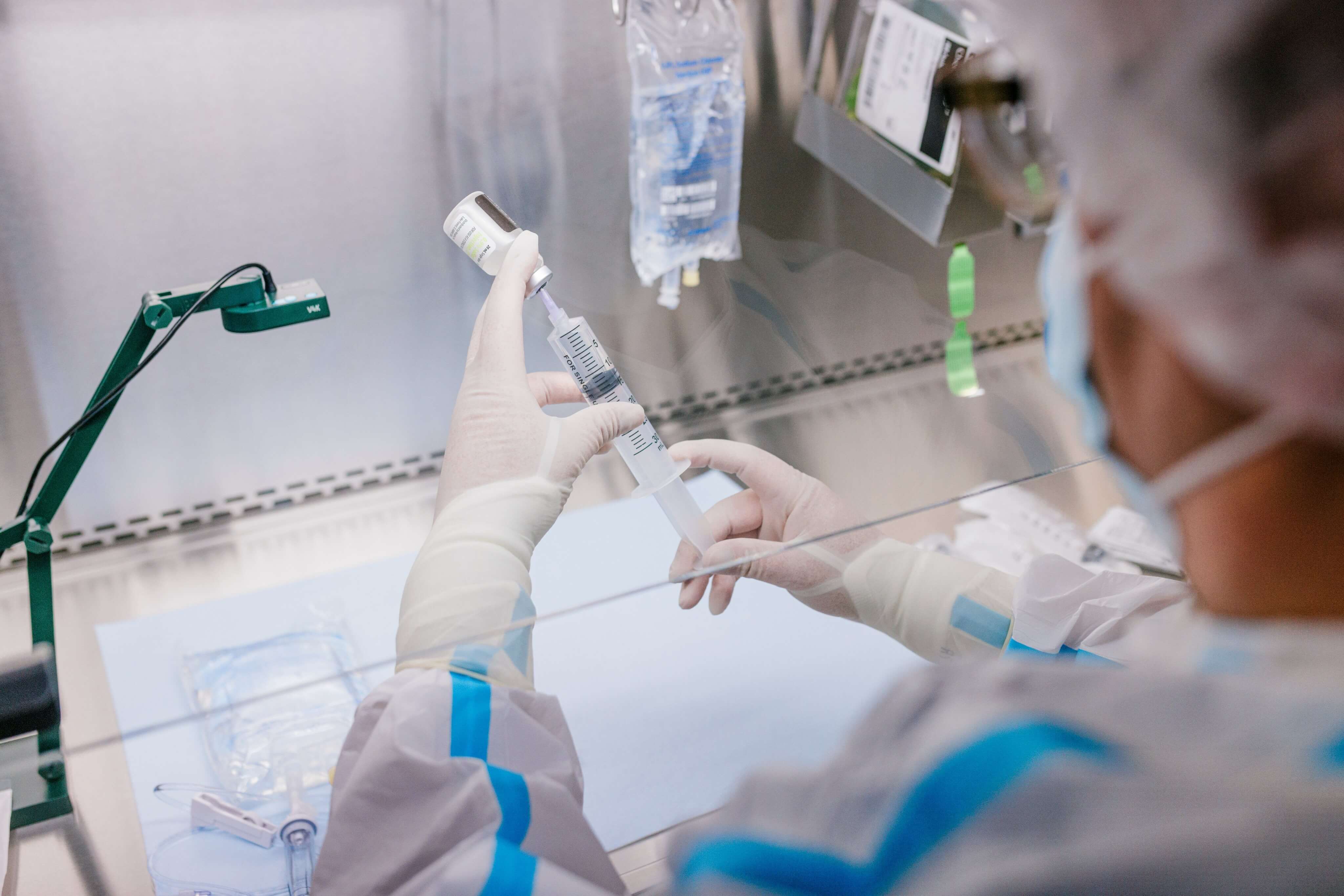 Healthcare professional in protective gear preparing medication with syringe in a sterile lab environment.