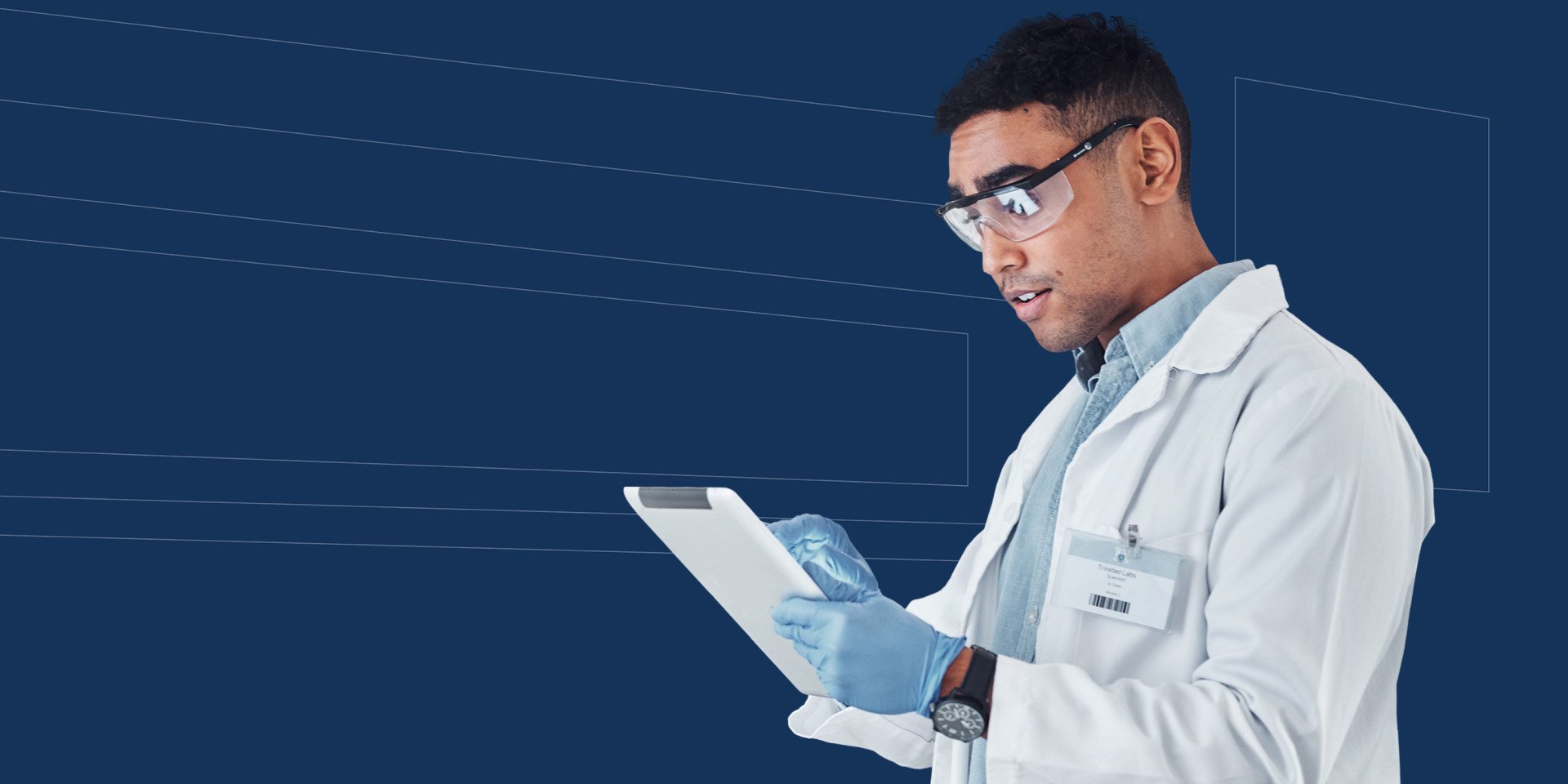A person in a white lab coat and blue gloves is holding and looking at a tablet against a solid blue background.