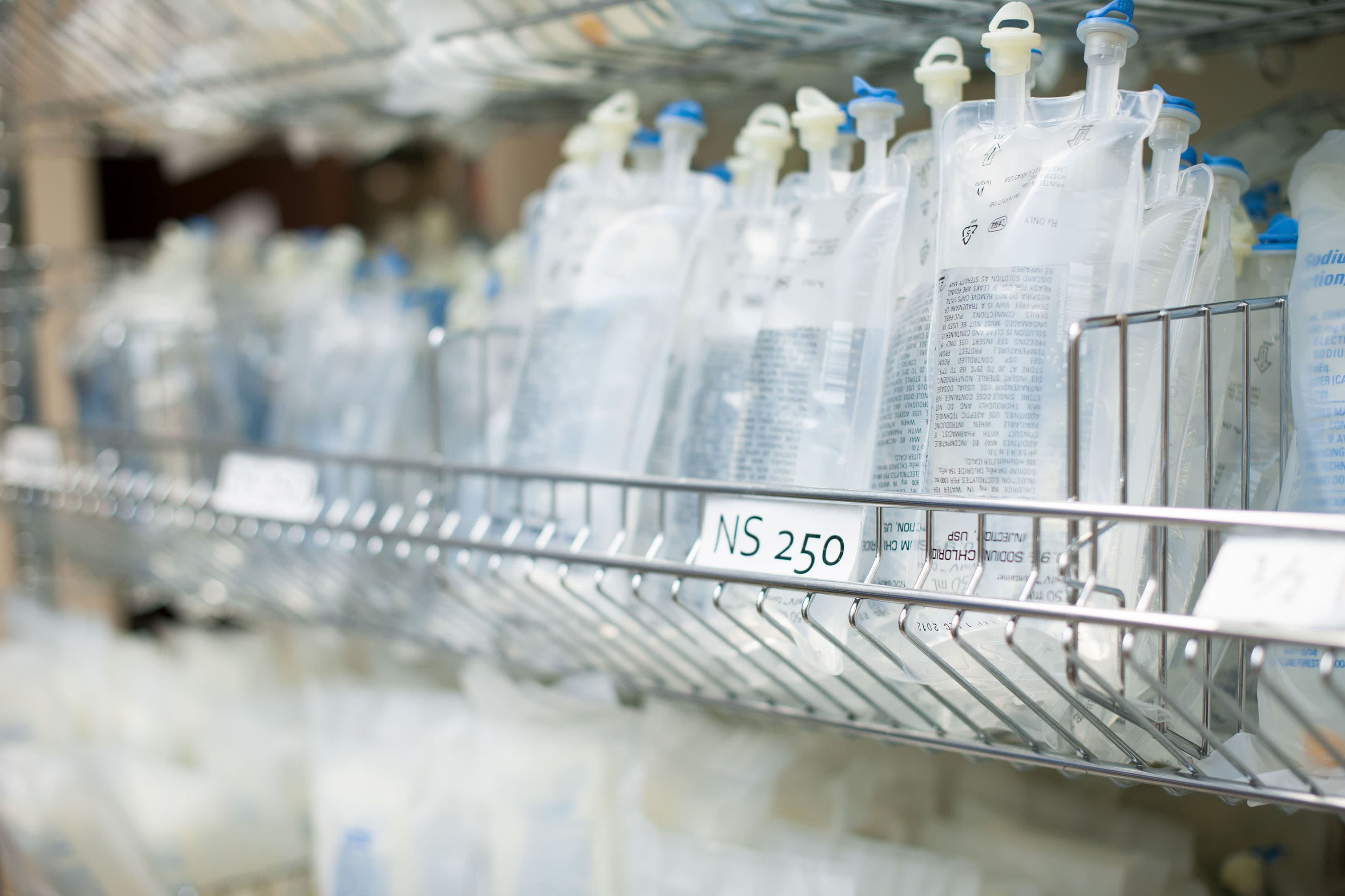 Shelves filled with multiple intravenous (IV) fluid bags labeled 'NS 250' in a medical storage area.