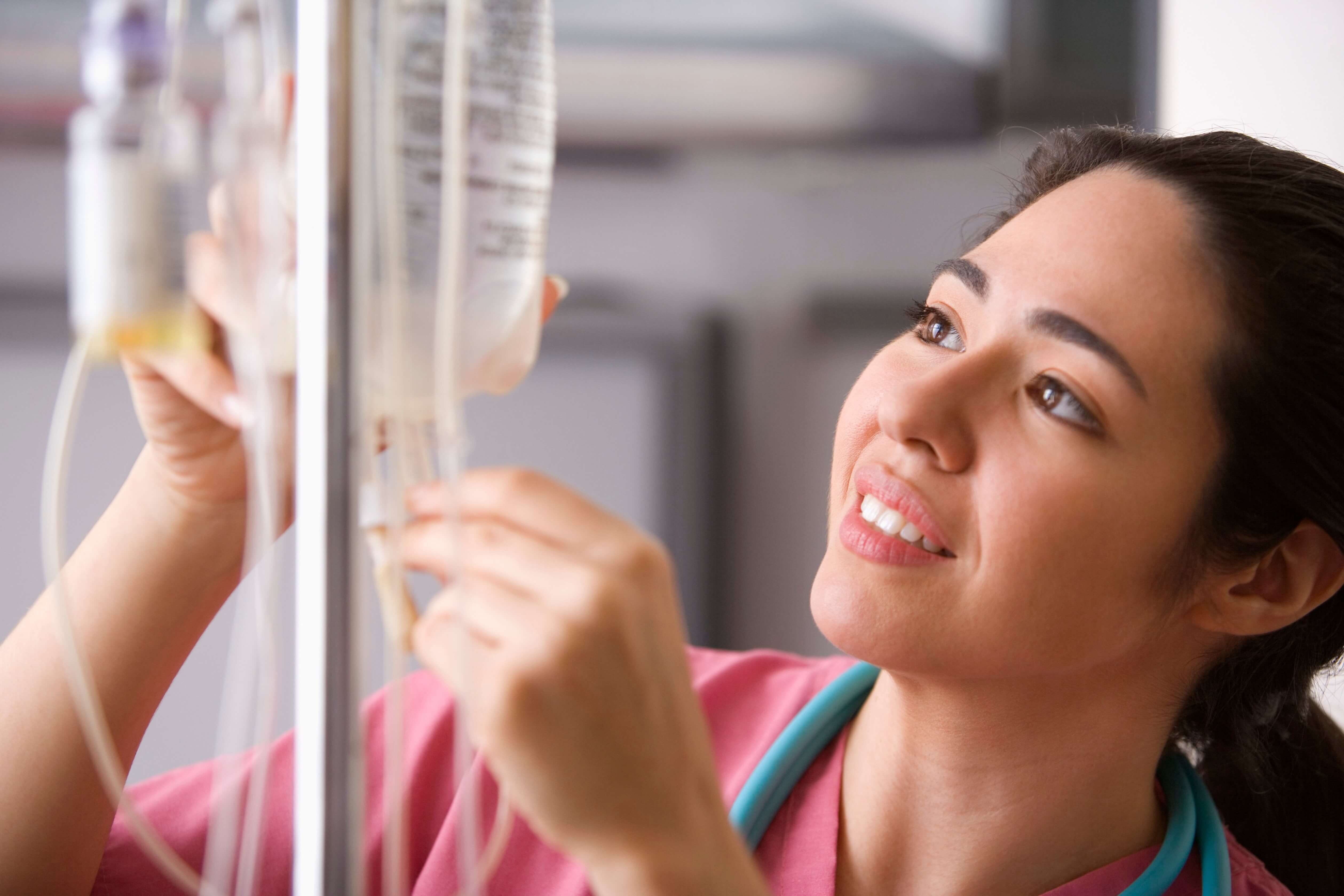 Healthcare worker in pink scrubs adjusting an IV drip.