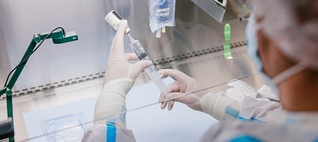 Scientist in protective gear preparing a syringe in a laboratory setting.