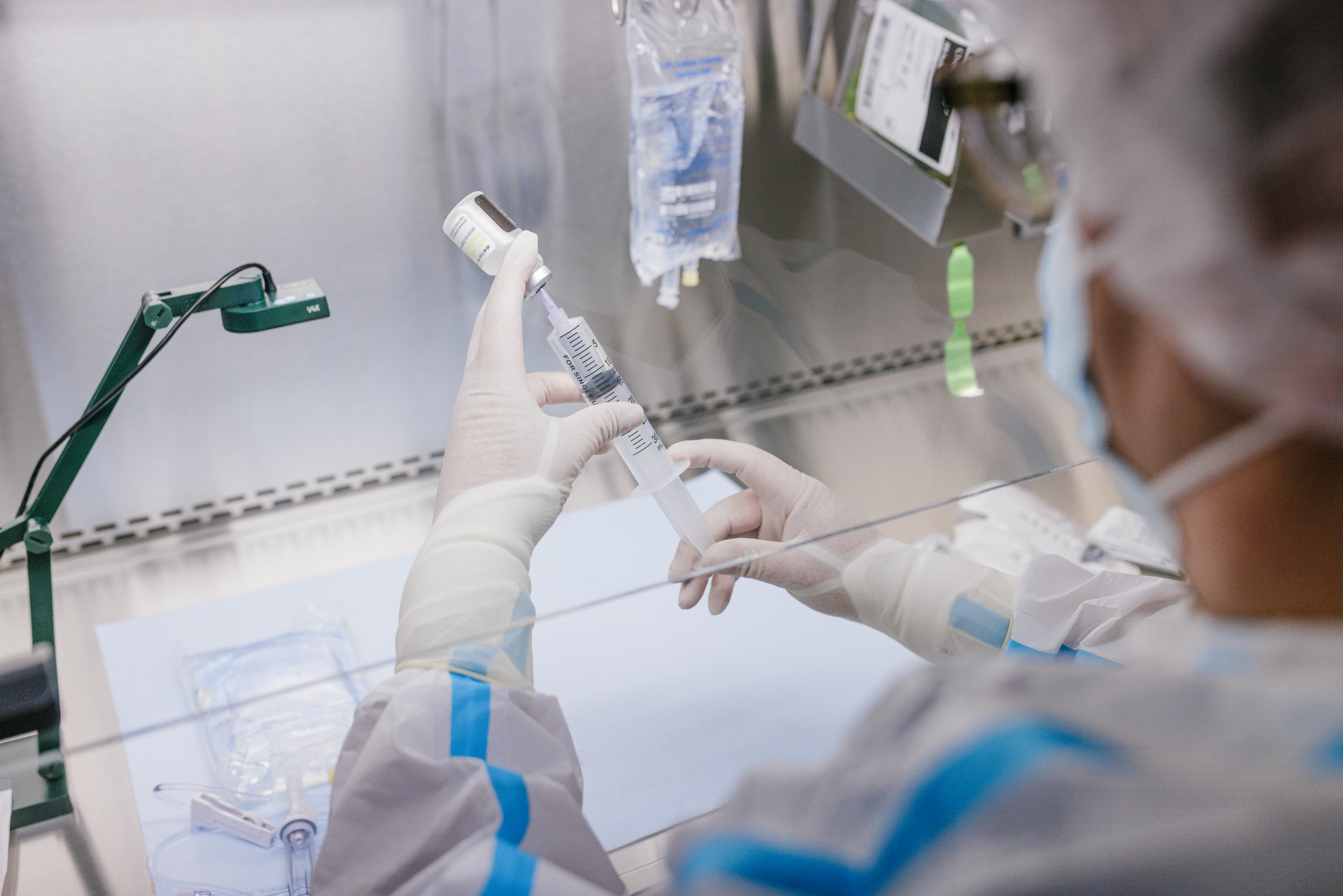 A lab technician in protective gear prepares a syringe with a liquid under a fume hood.