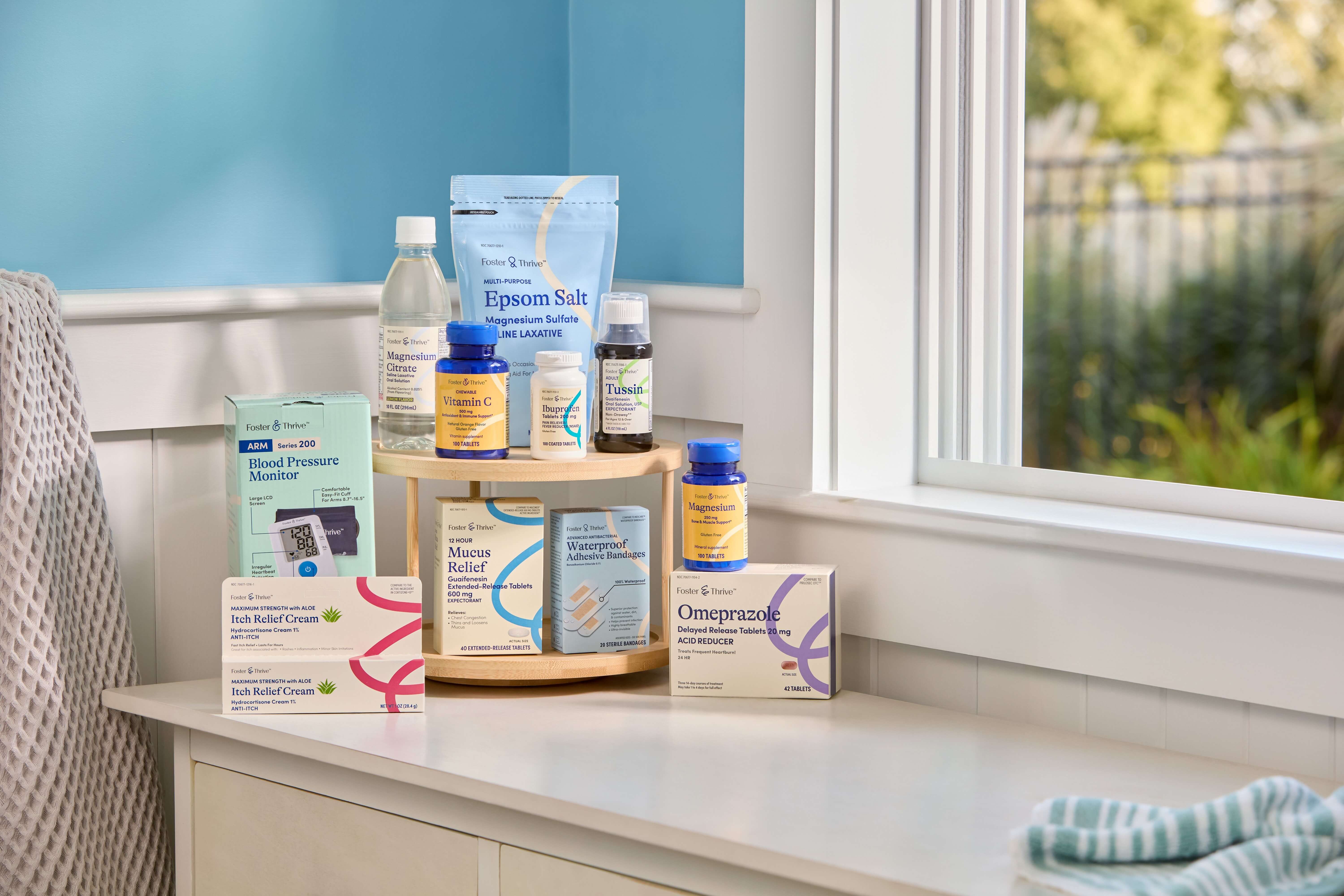 Various health and wellness products, including supplements, Epsom salt, and blood pressure monitor, arranged on a white surface near a window.