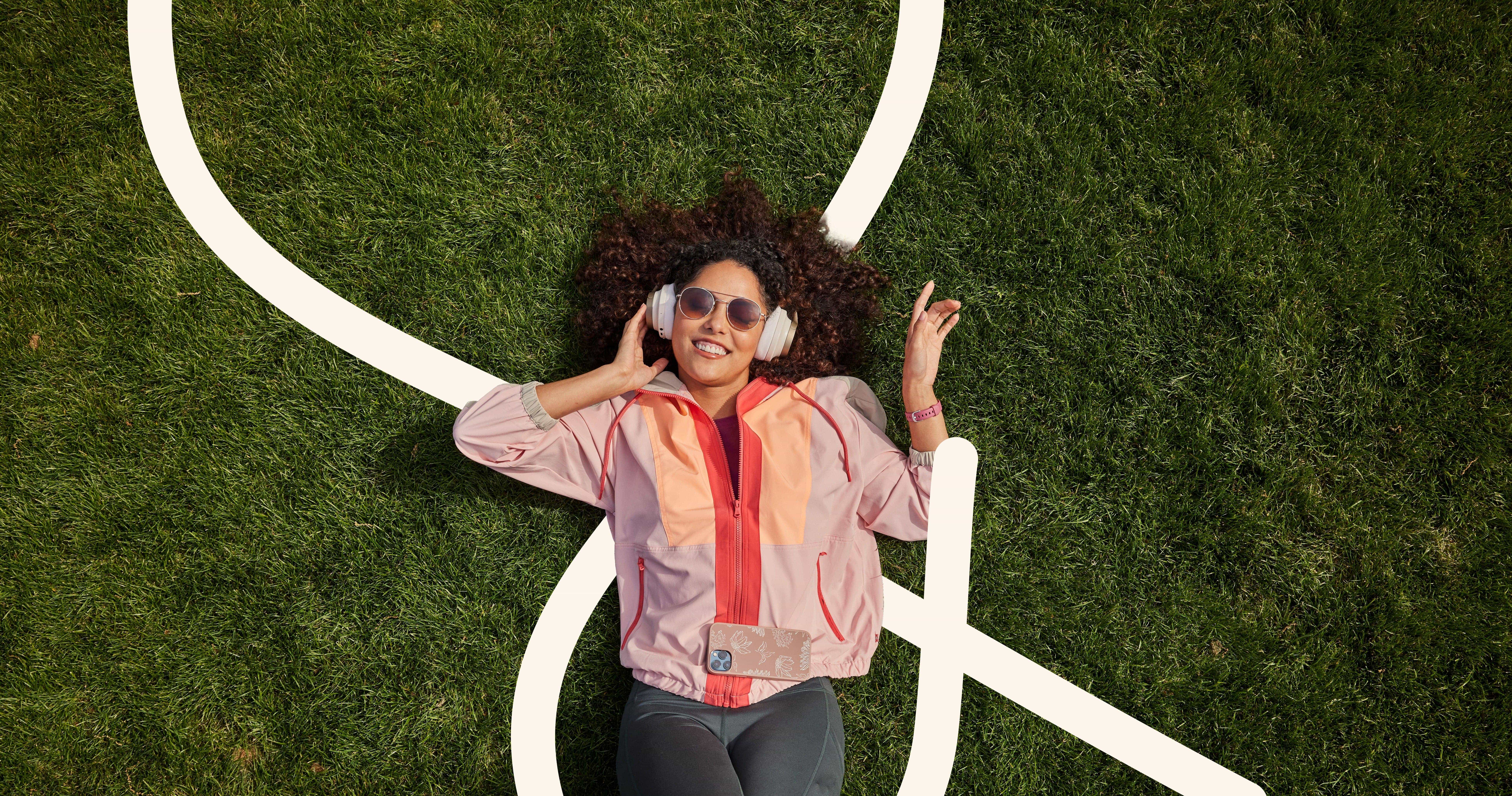 Person lying on grass with headphones, wearing a pink jacket, surrounded by a large white outline of the 'and' symbol.