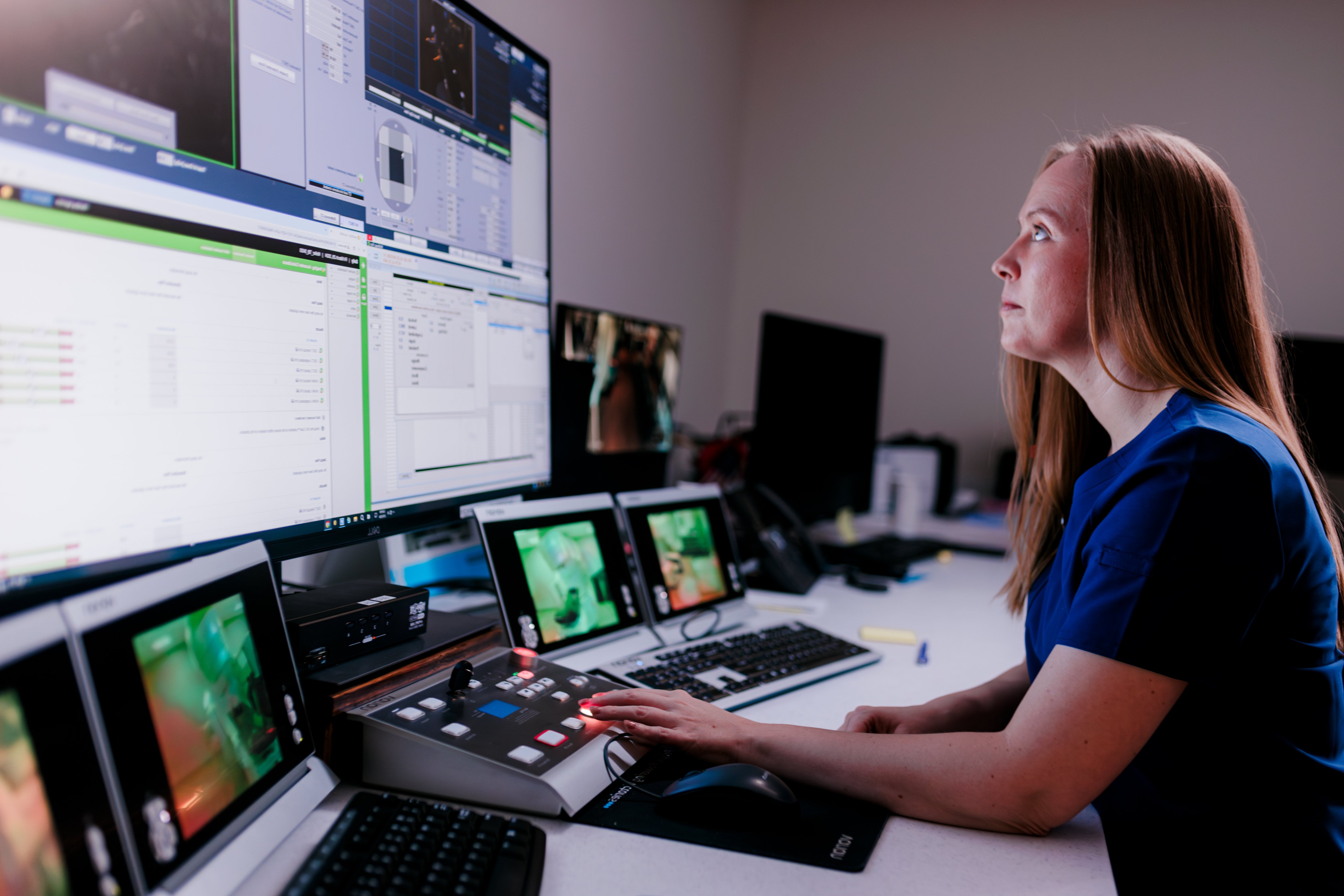 Person in a control room monitoring multiple screens and operating equipment.