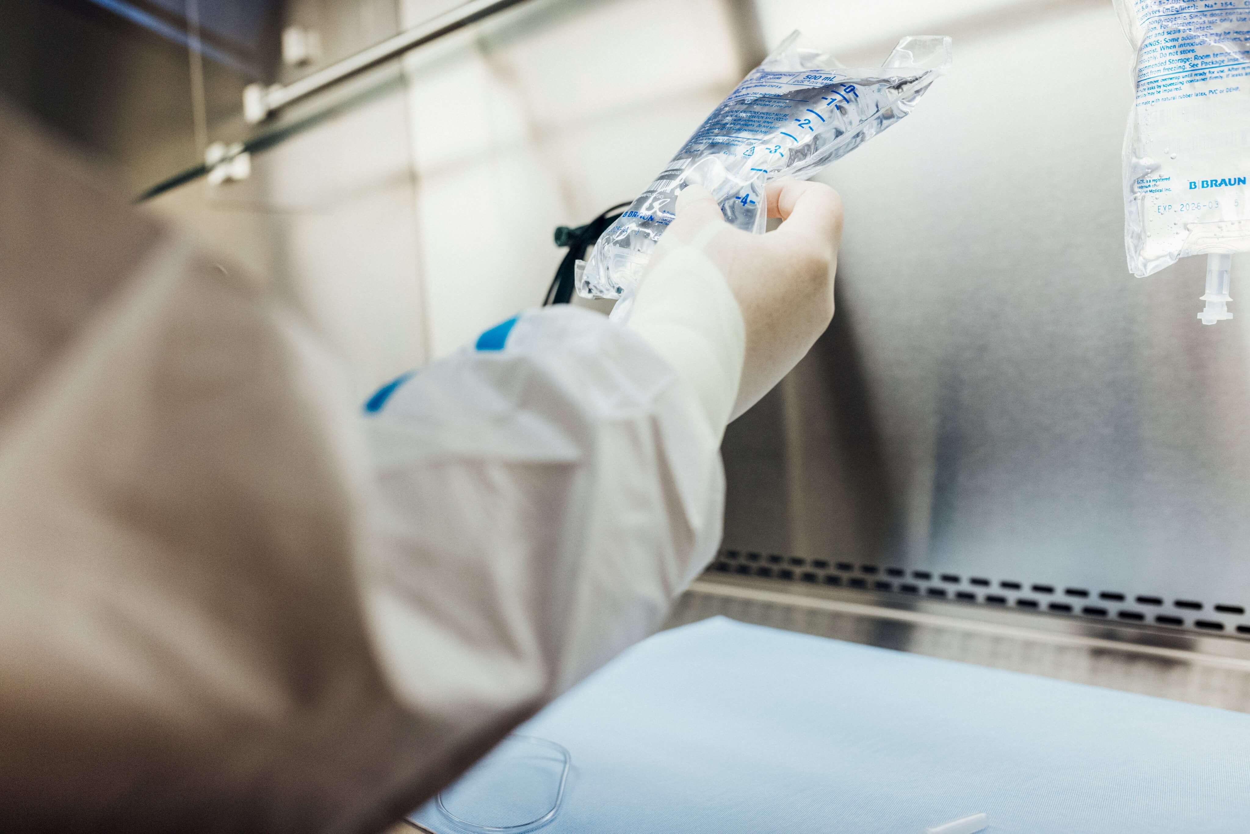A healthcare worker in protective gear handling an IV fluid bag in a sterile environment.