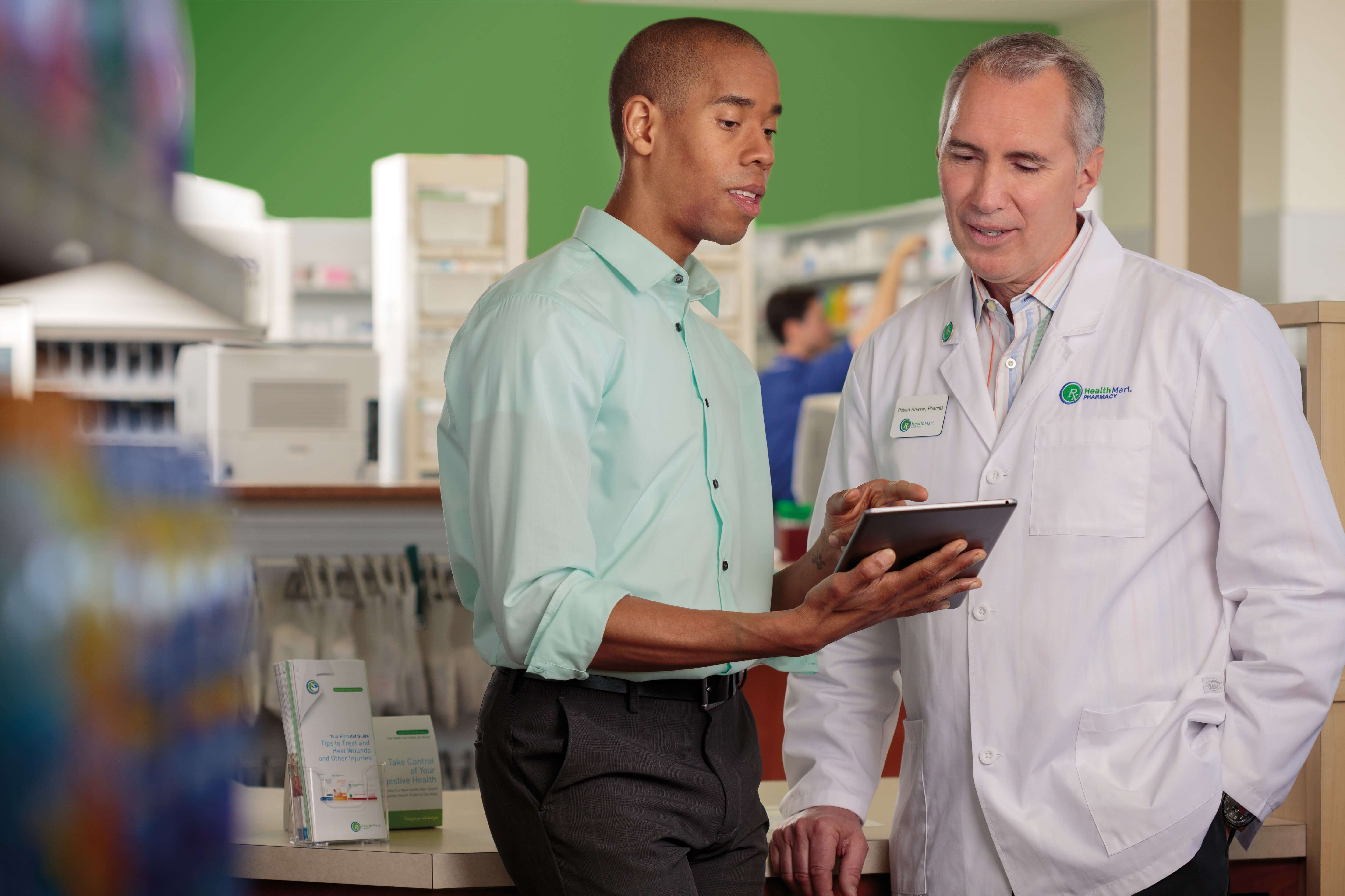 Two professionals in a pharmacy discussing something on a tablet.
