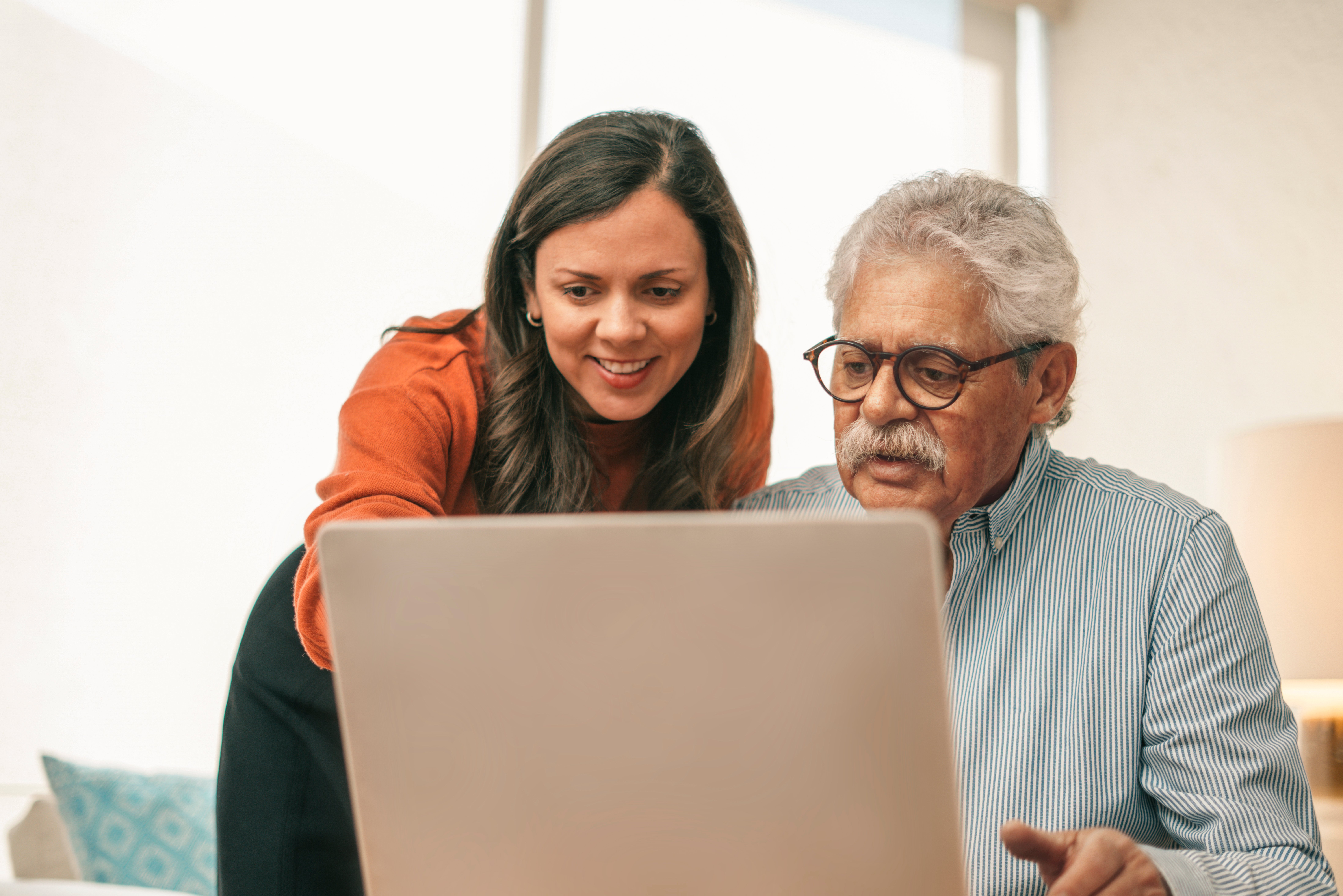 Two people looking at a laptop screen, one standing and pointing, the other sitting.