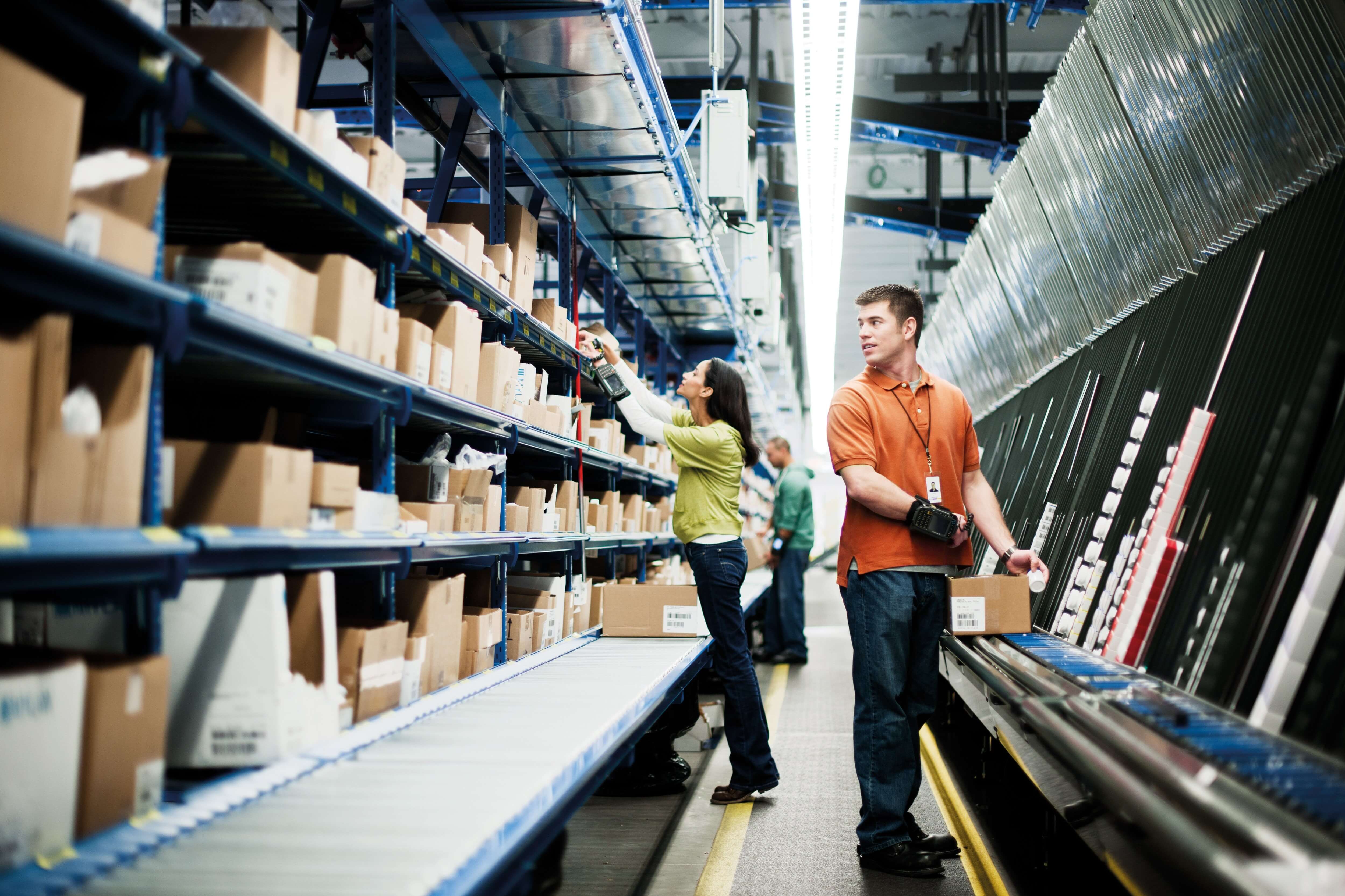 Workers in a warehouse picking items from shelves and placing them on a conveyor belt.