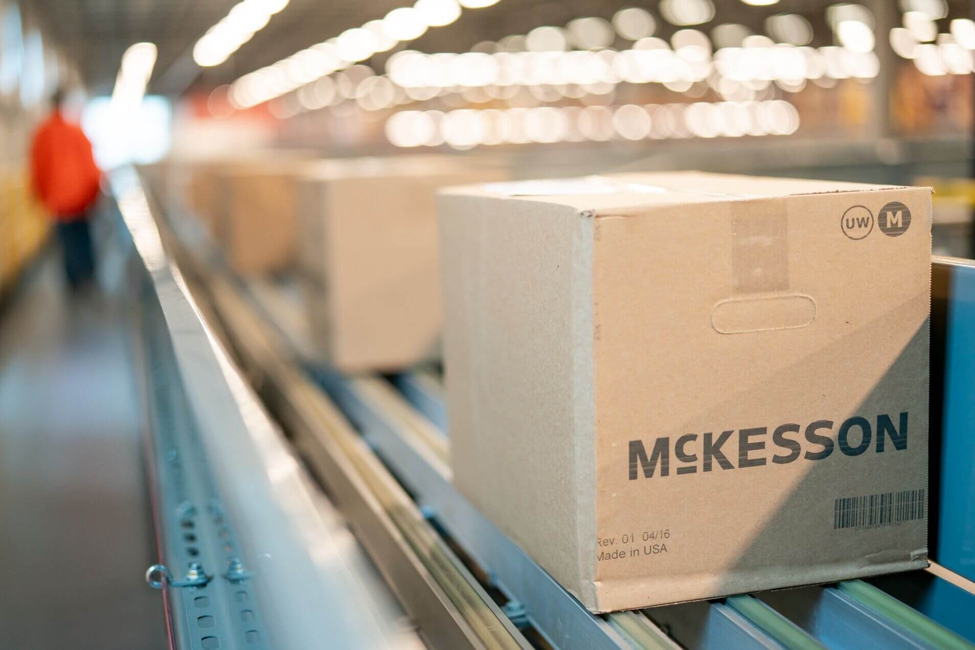 Cardboard boxes on a conveyor belt in a warehouse, with one box labeled 'McKesson' in focus.
