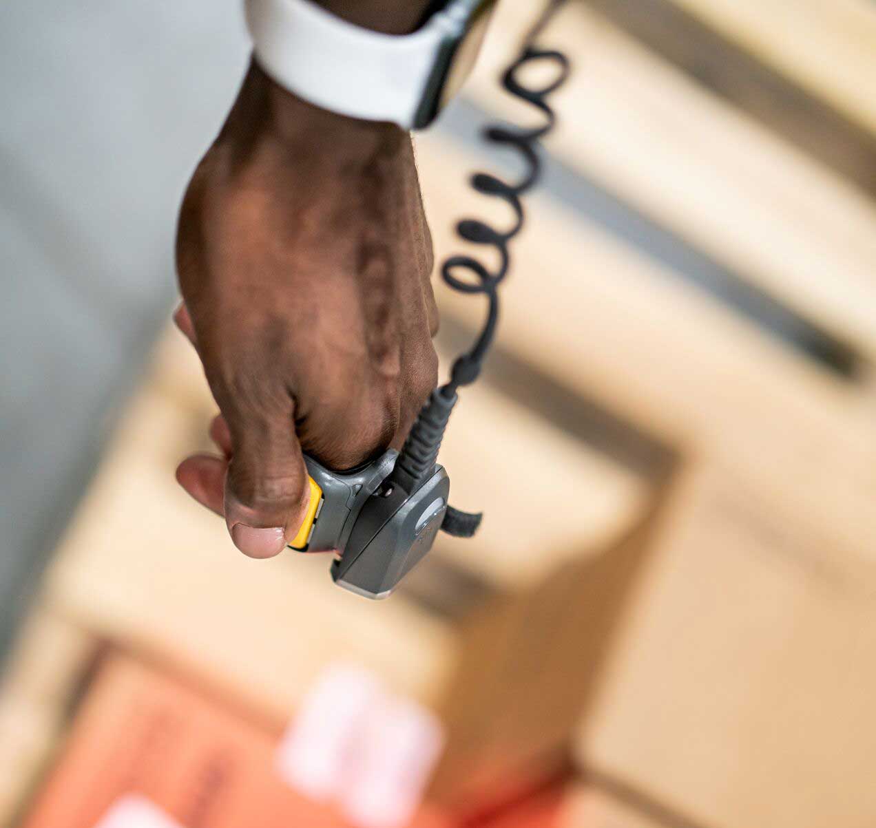 A hand holding a barcode scanner over cardboard boxes, one orange and one brown, with shipping labels.