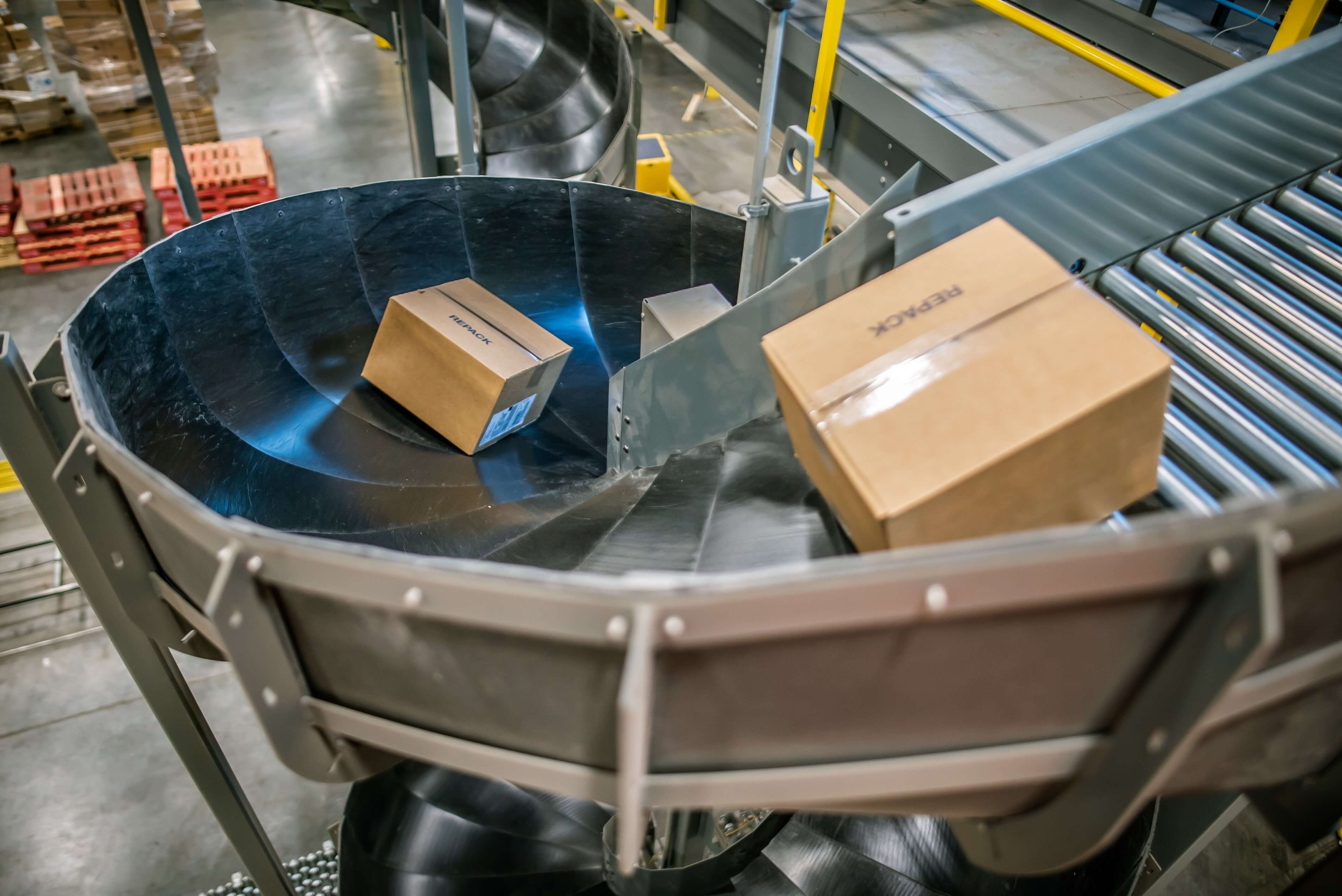 Two cardboard boxes on a spiral conveyor belt in a warehouse.