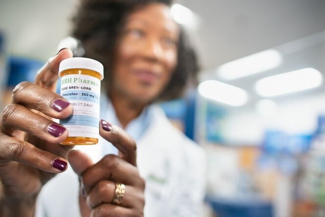 A person holds a prescription bottle labeled "ABH Pharma" with medication details visible.