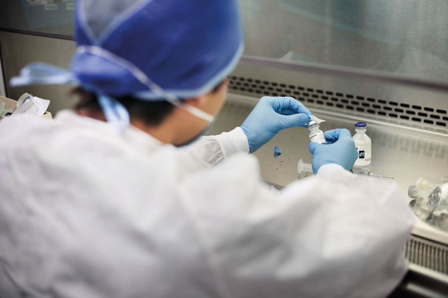 A lab technician in protective gear prepares a sample at a laboratory workstation.