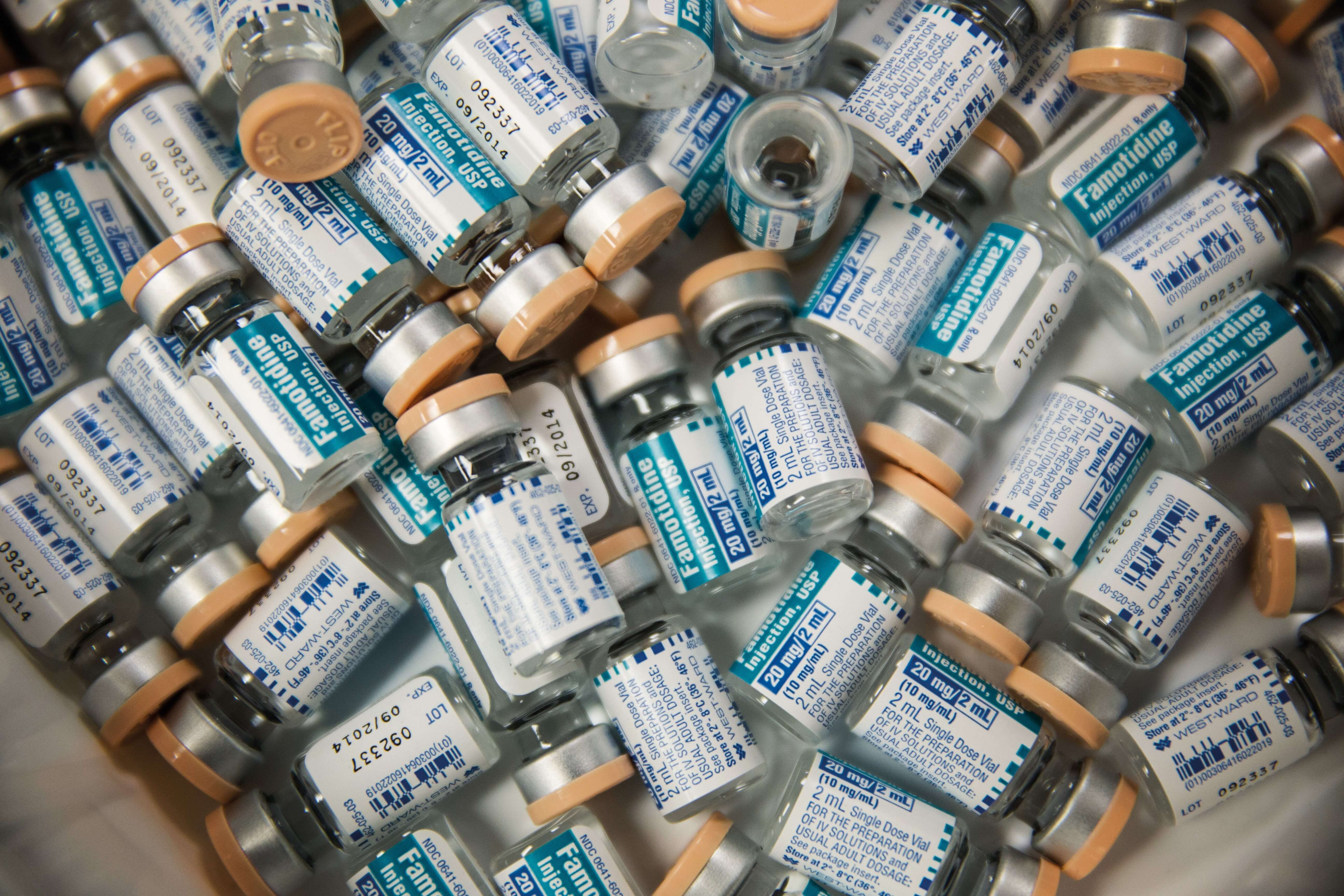 A pile of small medical vials with blue and white labels and orange caps.