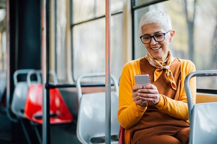 Person with short hair in yellow and brown outfit using a smartphone on public transportation.