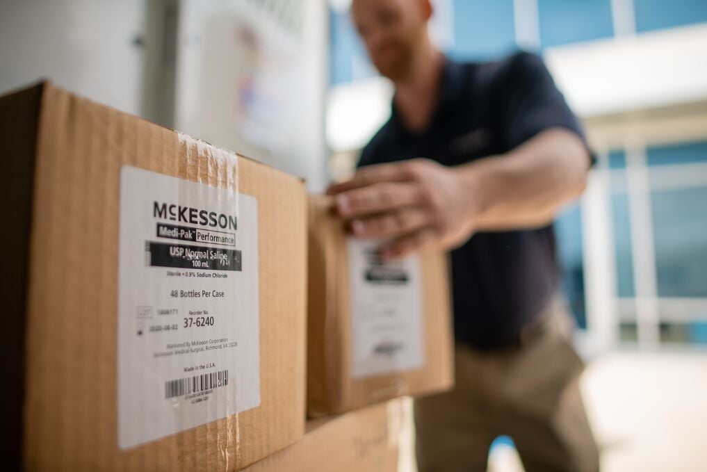 A person handling a cardboard box labeled "McKesson" with other boxes in the background.
