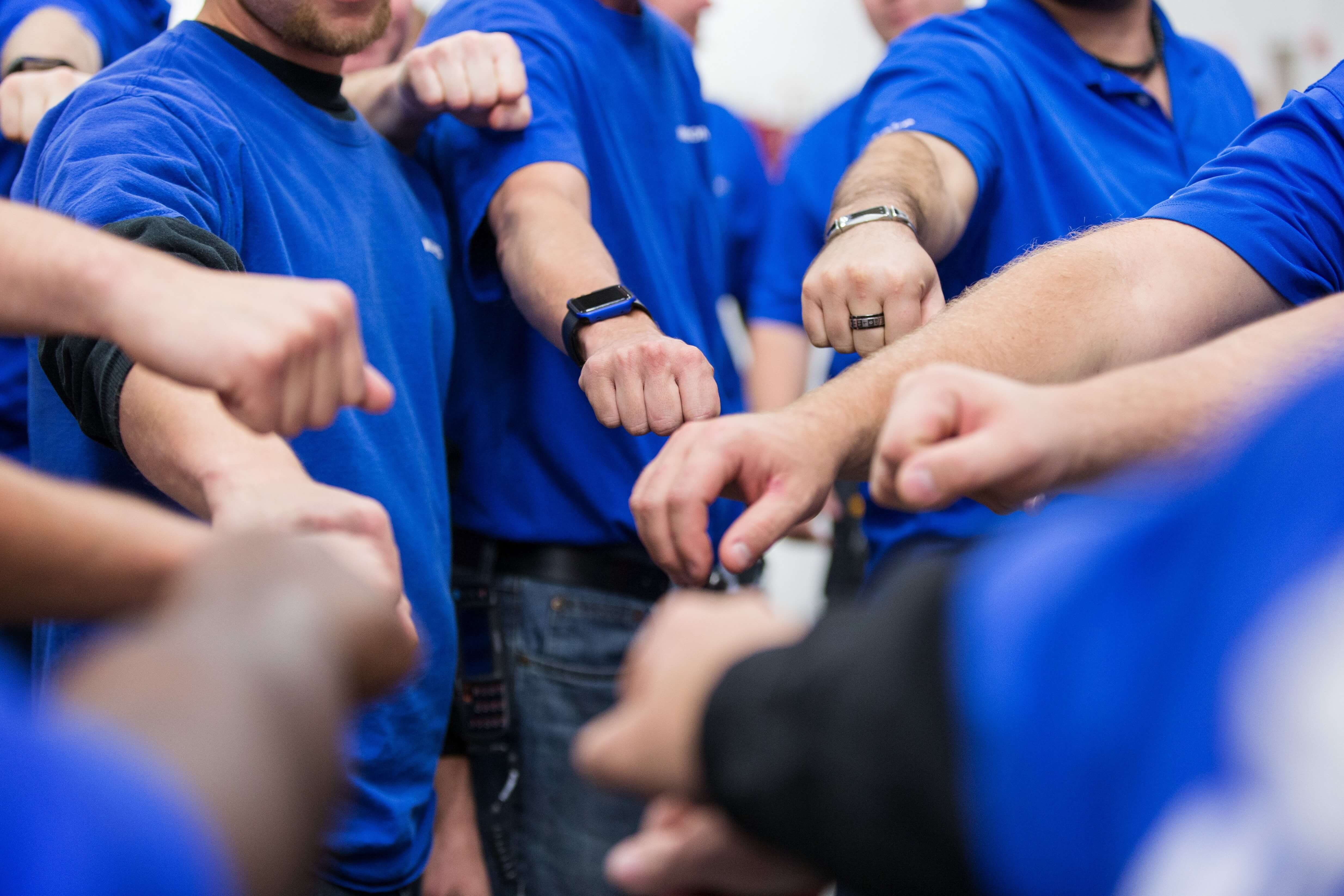 Group of people in blue shirts doing a fist bump.