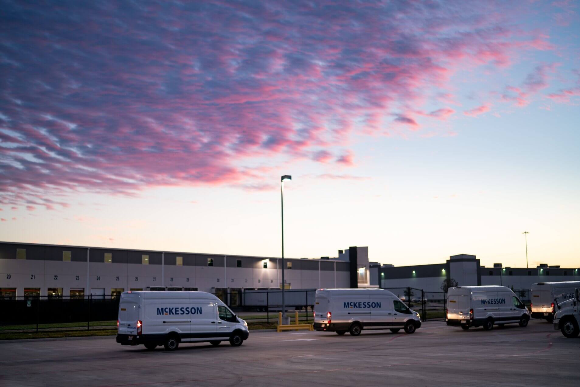 McKesson vans parked in a lot at sunset with a building and colorful sky in the background.