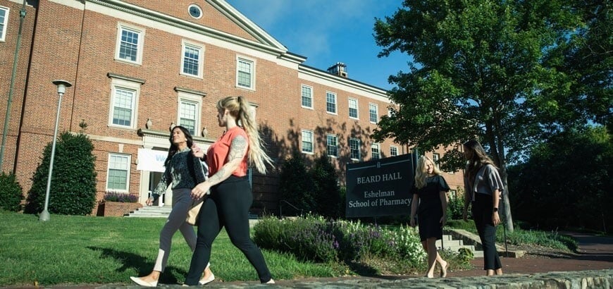 Four people walking in front of Beard Hall, Eshelman School of Pharmacy, on a sunny day.