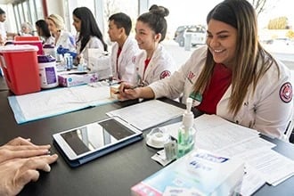 Medical students in white coats working at a table with documents and medical supplies.