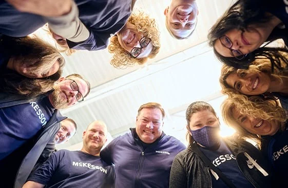 Group of people wearing "McKesson" shirts standing in a circle and looking down at the camera.