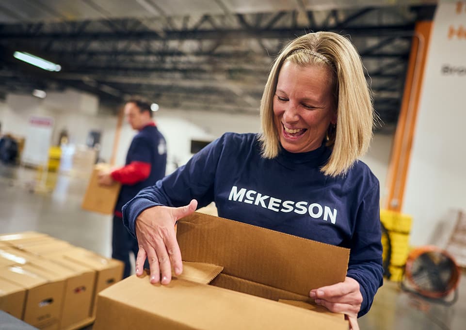 Person in a McKesson shirt packing a cardboard box in a warehouse.