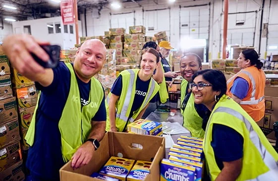 People in safety vests working in a warehouse, some taking a selfie.