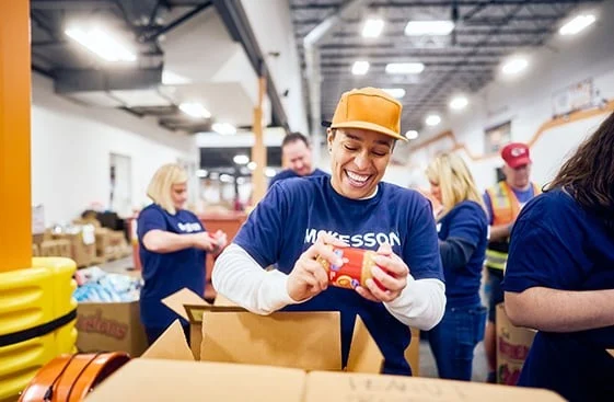 Volunteers in blue shirts pack food items into boxes at a warehouse.