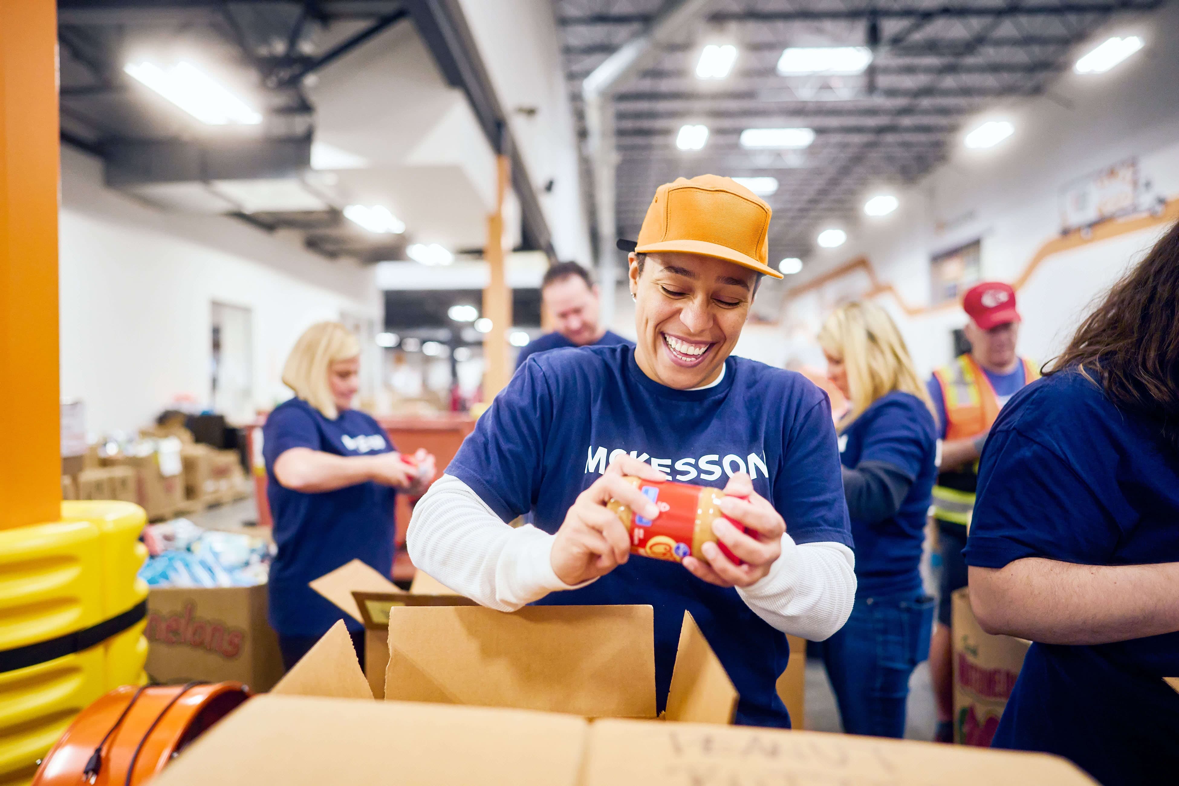 Volunteers in blue shirts pack food items into boxes at a warehouse.
