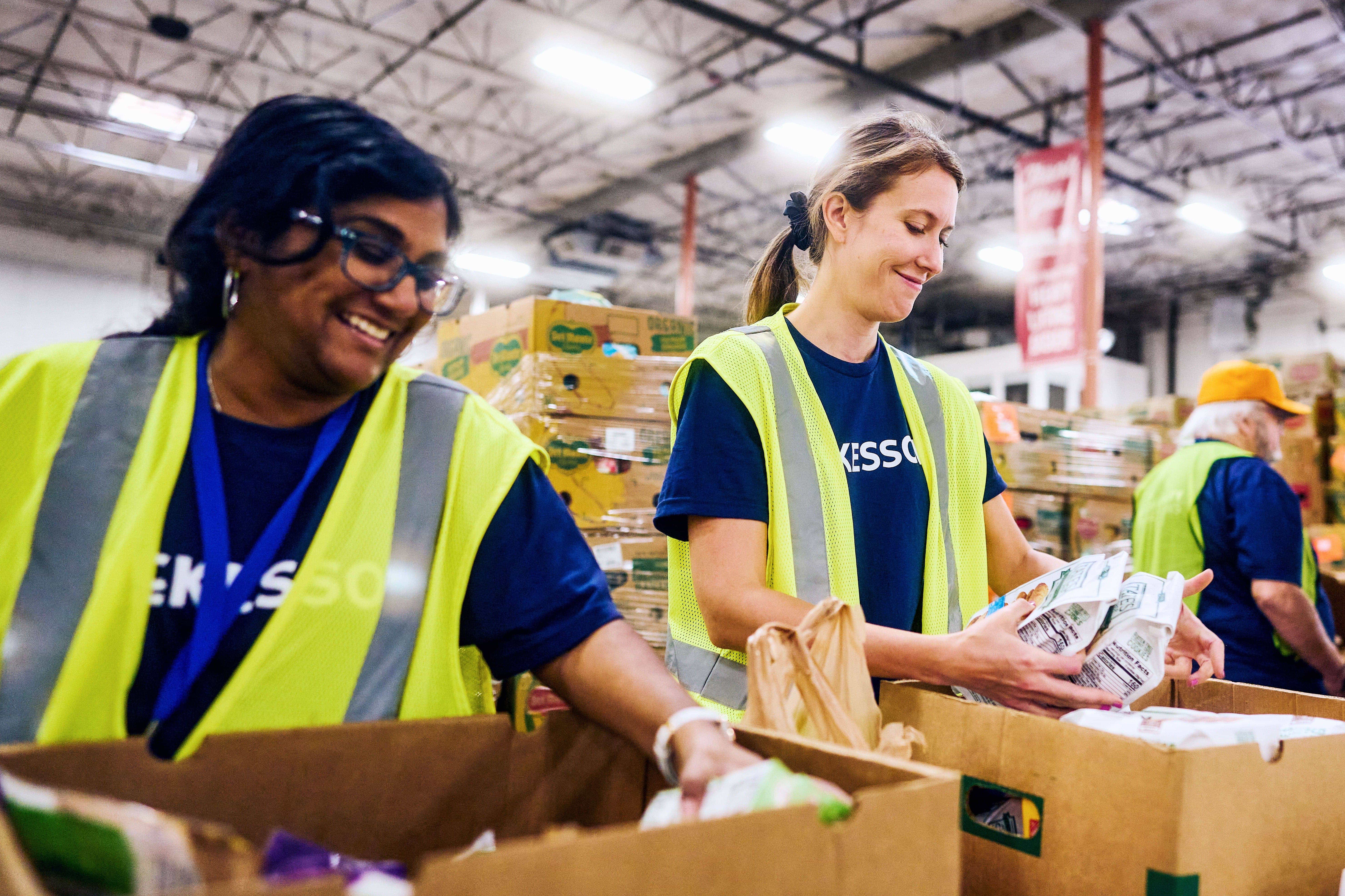 People wearing reflective vests sorting food items into boxes in a warehouse.