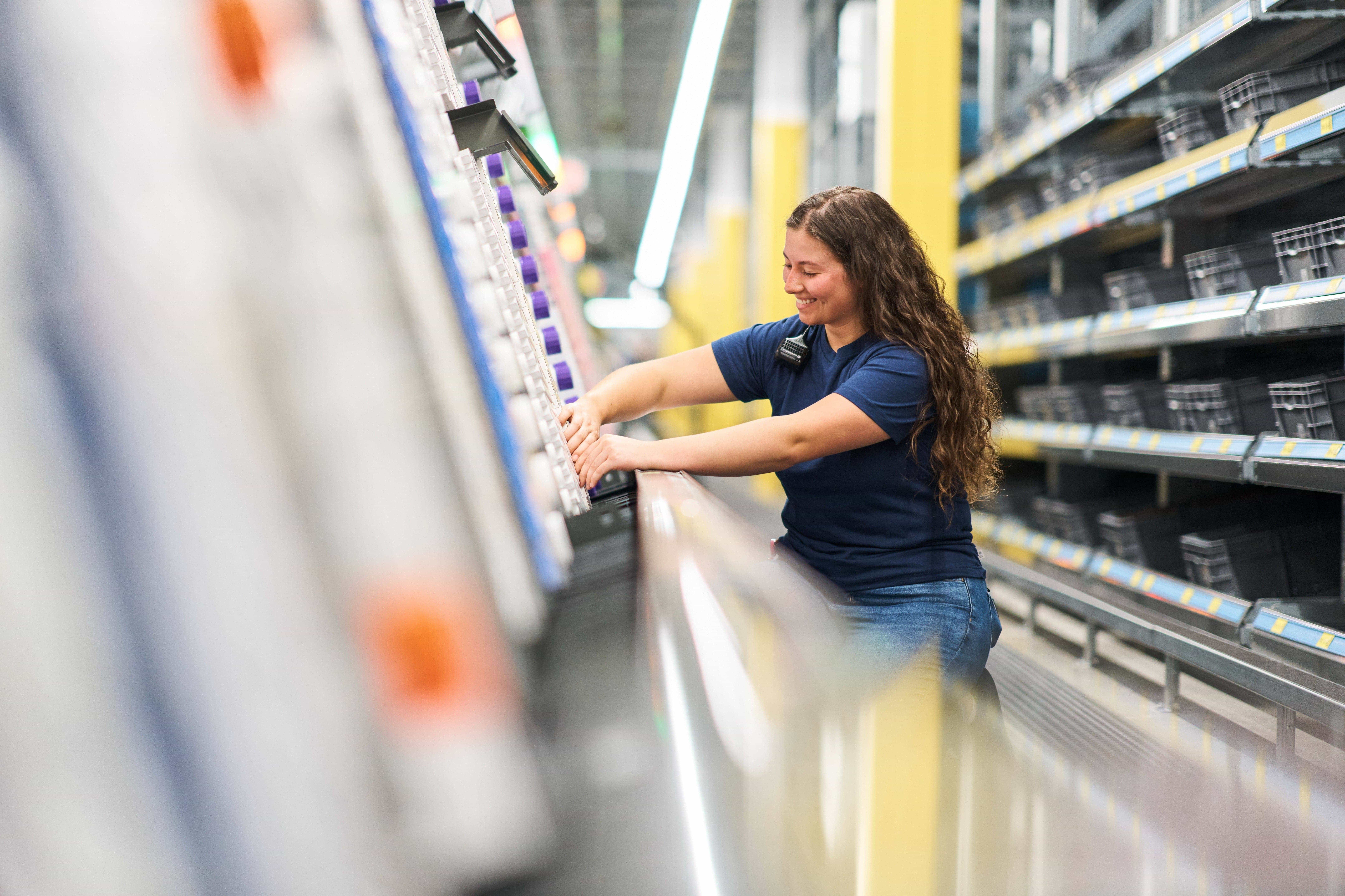 Person in a blue shirt stocking shelves in a store aisle with empty shelves on the right.
