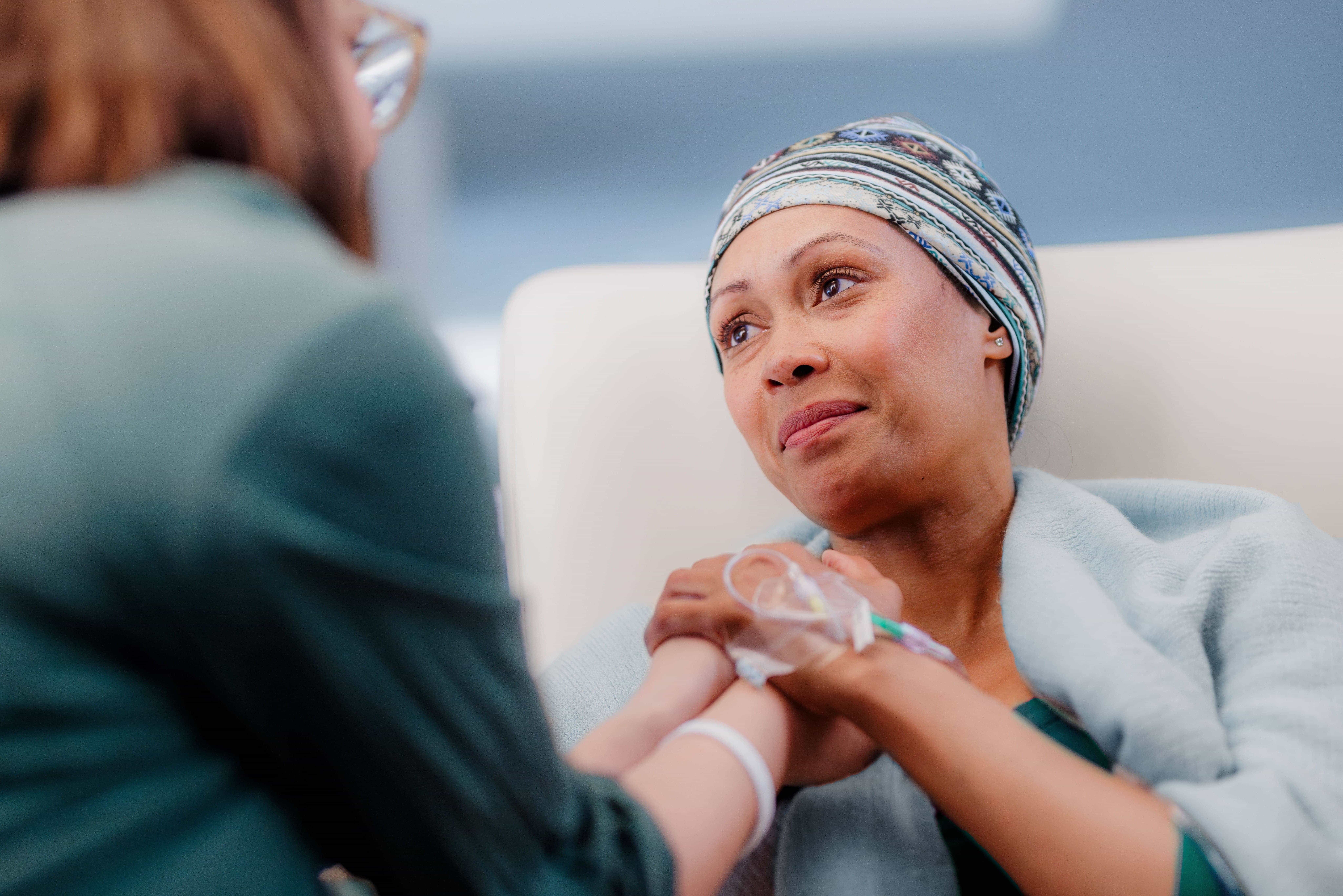 A person with a headscarf receiving support while undergoing an intravenous treatment.