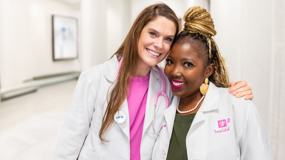 Two healthcare professionals in white coats standing together in a hospital corridor.