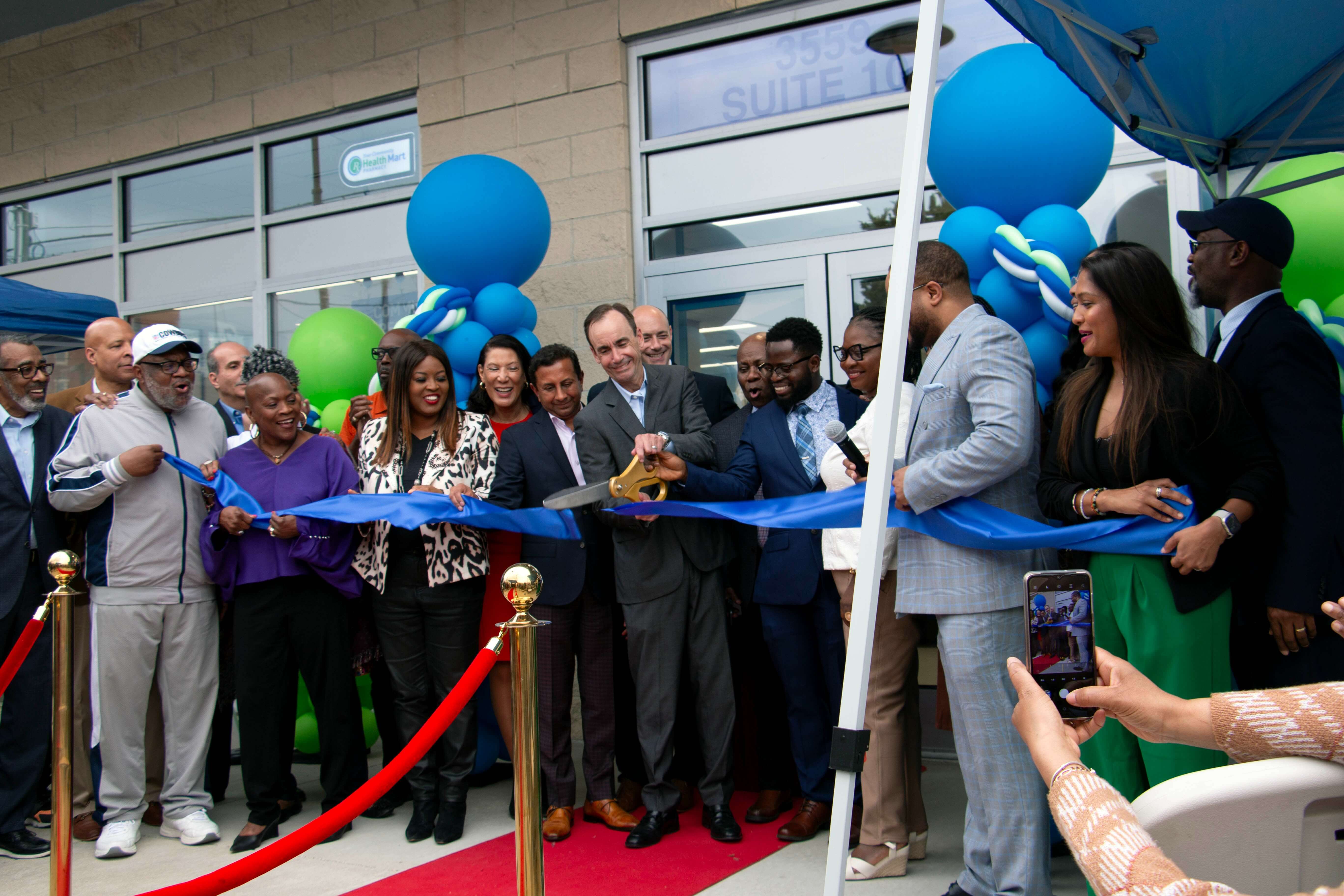A group of people cutting a blue ribbon at an outdoor event in front of a building.