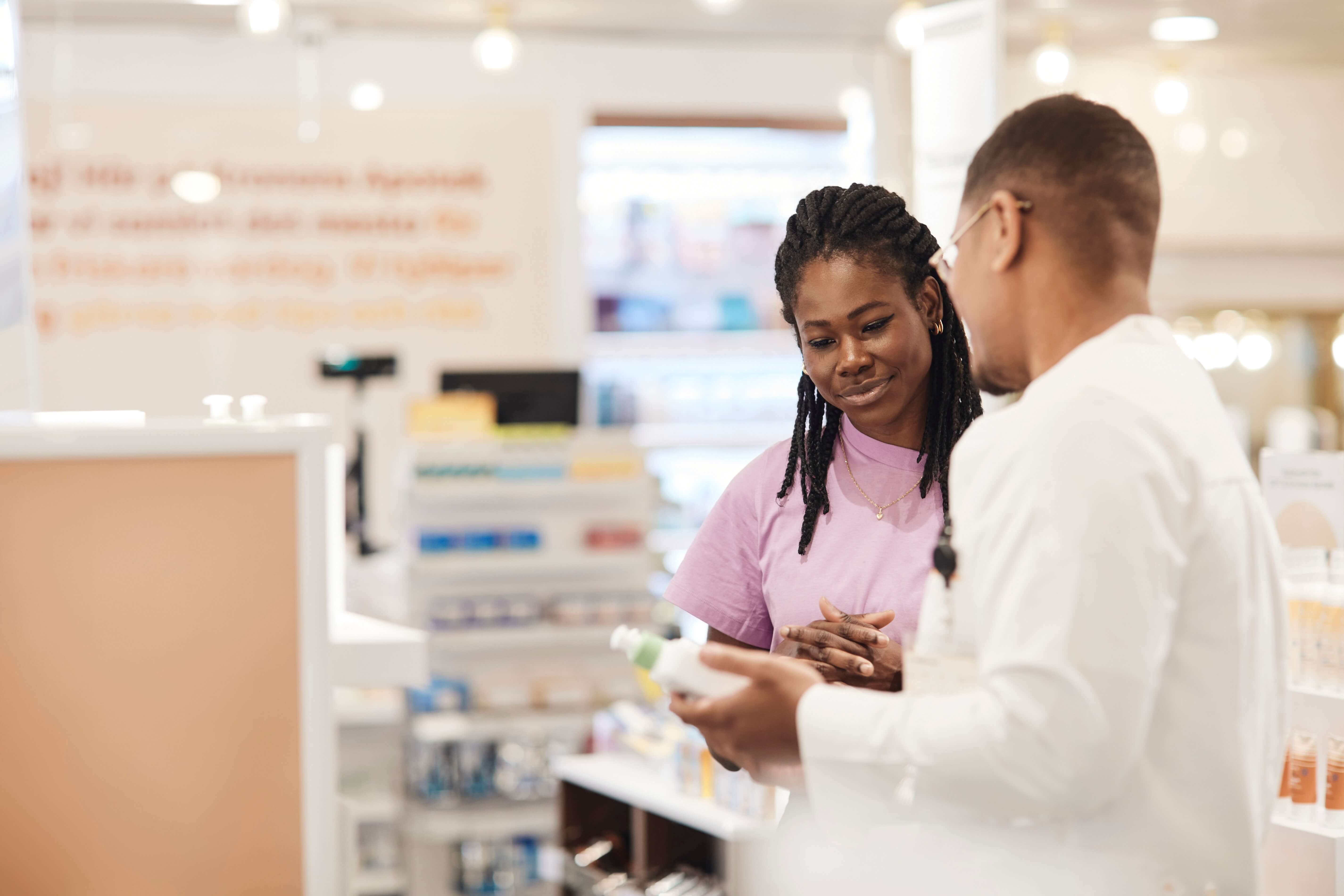 Two people talking in a pharmacy, one holding a product.