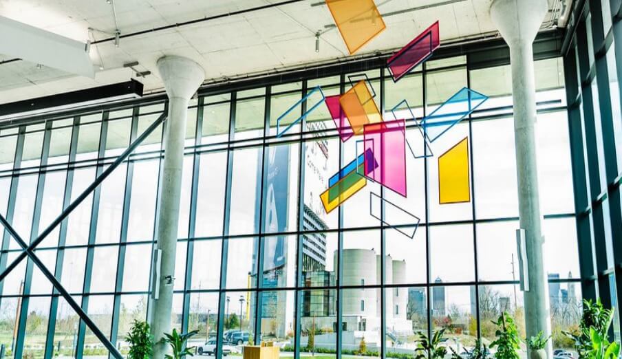 Modern building interior with large windows and colorful geometric shapes hanging from the ceiling.