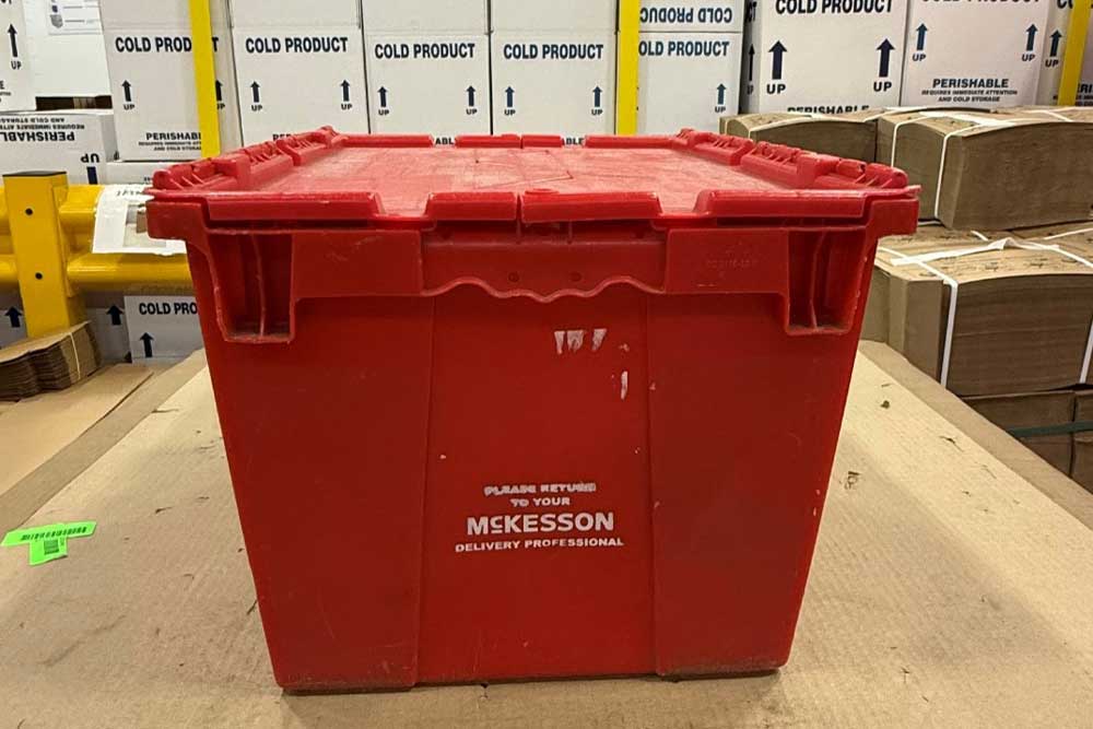 Red McKesson plastic bin on a cardboard surface in a warehouse with labeled boxes in the background.
