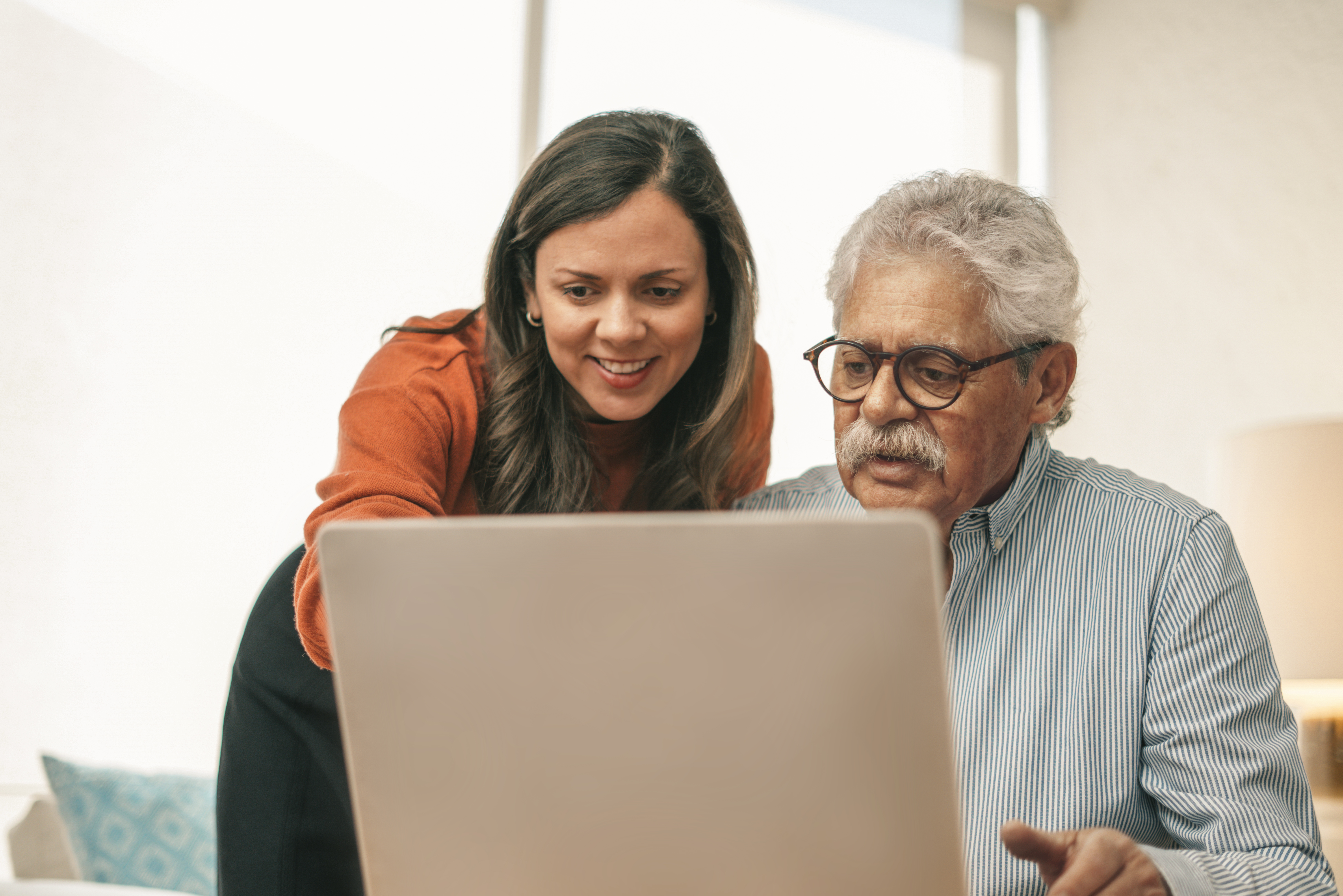 Two people looking at a laptop screen together, one standing and pointing, the other sitting.